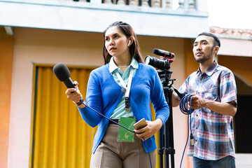 a beautiful reporter in blue cardigan with green name tag hunting for news with a cameraman behind...