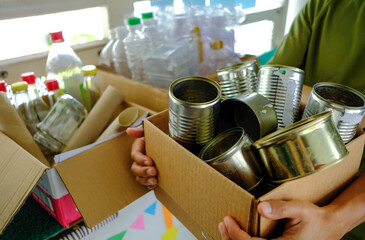 Zero waste sustainability concept. Man holding brown carton box of metal cans to be recycled outside HDB flat. Sorting boxes for plastic glass bottles containers paper in background. Selective focus.