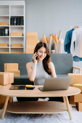 Obraz premium Startup small business SME, Entrepreneur owner woman using smartphone or tablet taking receive and checking online purchase shopping order to preparing pack product box. .