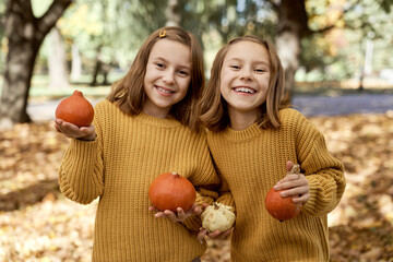 Child siblings standing in the woods and holding pumpkins