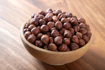Top view of a bowl full of peeled hazelnuts on wooden table