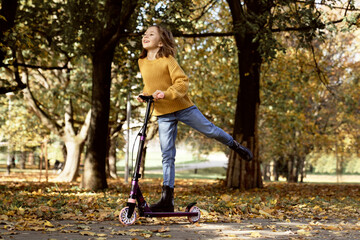 Caucasian child having fun in the woods while driving a push scooter