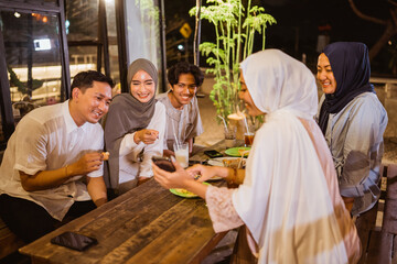portrait of a group of Muslim friends looking at mobile phones together while breaking fast at an...