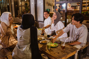 Muslim woman wearing hijab and Muslim man joking while breaking fast with friends at outdoor cafe