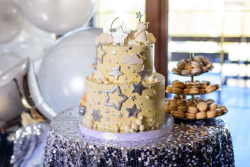 Yellow birthday cake decorated stars and macarons on candy bar.