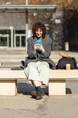 Happy woman commuter texting on phone sitting on bench outside