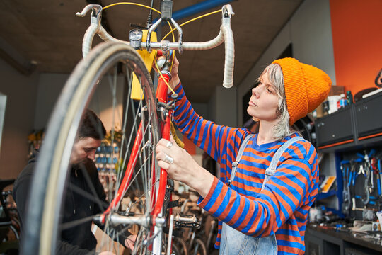 Smiling female bike mechanic repairing bicycle in workshop - Powered by Adobe