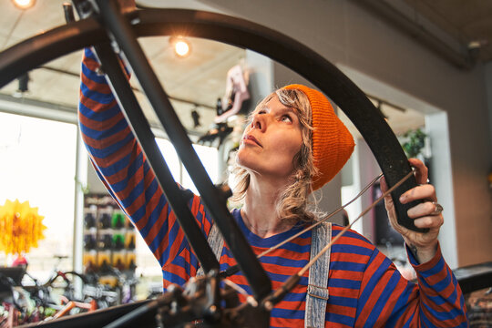 Involved woman bike mechanic examining and repairing bicycle in workshop - Powered by Adobe