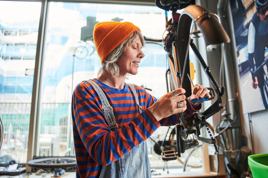 Positive woman cycling mechanic fixing bicycle and checking wheel spoke in workshop