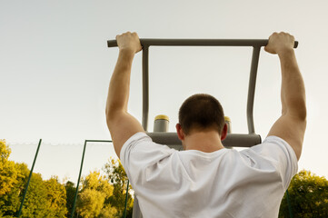 Man near pull-up bar. fitness. Unrecognizable caucasian men pull-up outdoor workout cross-training white t-shirt back view. Stretching arm before exercising. Young adult male fit body