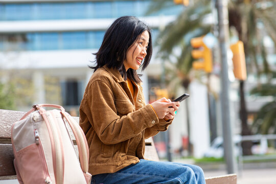 young asian woman using mobile phone while sitting on bench