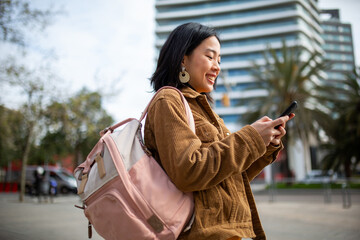 Fototapeta premium Side portrait of student with bag looking at mobile phone