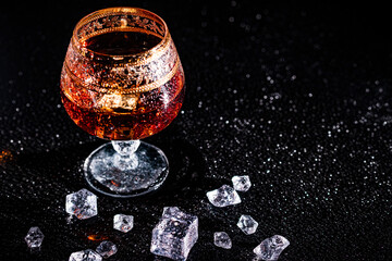 Glass with cognac and ice on a dark background. the concept of alcoholism and drinking