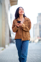 smiling young asian woman walking in city with cellphone