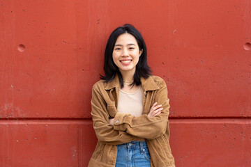 young asian woman smiling by wall with arms crossed