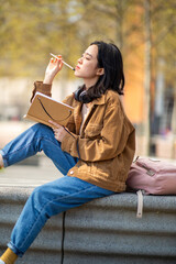young thinking woman sitting outside with book