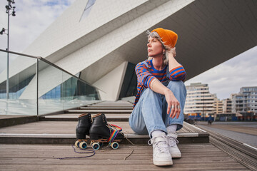 Dreamy adult woman sitting after roller skate riding and looking away while relaxing
