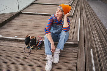 Dreamy adult woman sitting after roller skate riding and looking away while relaxing