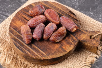 stalked dates on a teakwood cutting board on burlap. Ramadan iftar dishes. kurma tangkai. Tunisian dates. Deglet Nour Dates.