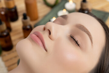 Face of young woman on spa procedures, bottles with cosmetics, wooden background, close up