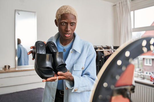 Multiracial hipster guy holding shoes while recording fashion social media channel blog