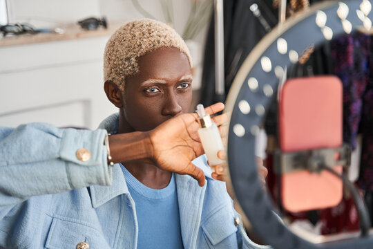 Multiracial blonde man filming makeup tutorial in front of smartphone camera at home
