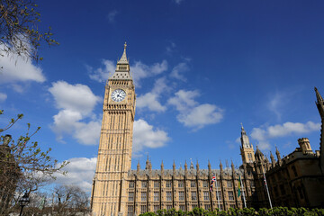 Big Ben Clock Tower in London and houses of parliament, UK, in a day with white clouds and blue sky.