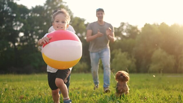 happy family. children and parents run in the park play ball. happy family kid concept. boy runs on grass in park holding the ball. group of children and parents family play in the park run dream