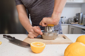 Man in sportswear squeezing lemon juice in the kitchen.