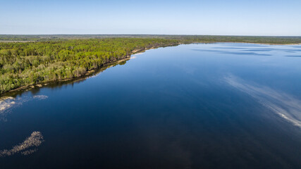 panoramic aerial view of the lake and the green meadow with buildings taken from a drone in summer