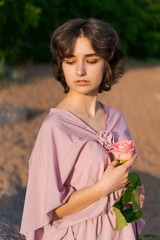 portrait of a romantic girl in a pink dress with a rose in her hand on the seashore at sunset