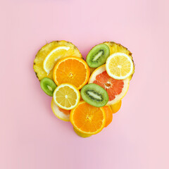 Fruit heart made of pineapple, grapefruit, orange, lemon and kiwi slices against bright pink background. Copy space. Creative summer idea. Minimal fruit concept.