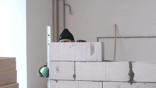 The builder places a level against the wall to check that it is level while the wall is being erected.