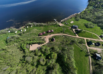 panoramic aerial view of the lake and the green meadow with buildings taken from a drone in summer