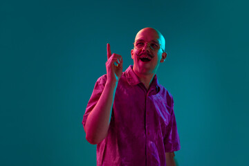 Portrait of young bald man with moustache and trendy unglasses generating creative ideas against cyan studio background in neon light. Concept of human emotions, facial expression, lifestyle