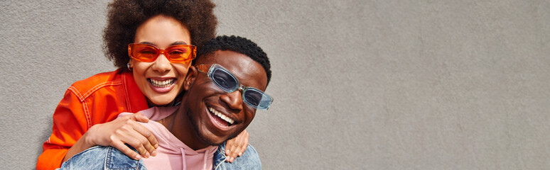 Cheerful african american woman in modern sunglasses and bright outfit hugging best friend and...