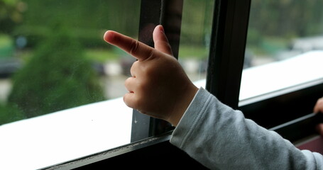 Little boy standing by window pointing outside with hand and finger
