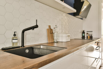 a modern kitchen with white hexagon tiles on the wall and wooden countertop, black tap fauce