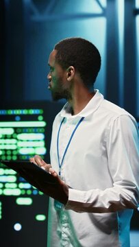Vertical video IT programmer in server hub using tablet to find firewall misconfigurations affecting mainframes performance and connectivity, leading to slow data transfer rates and poor client