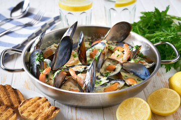 Mussels clams  in cream sauce in cooking pan and toasted bread on wooden table.