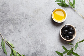 Black olives and extra virgin olive oil in little bowl with olive tree branches top view on gray...