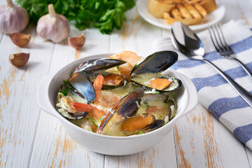 Creamy soup with seafood on a white wooden table.