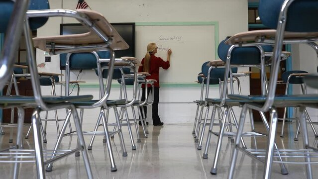 Wide angle view of woman teacher using an interactive whiteboard blackboard in an empty classroom teaching geometry math.