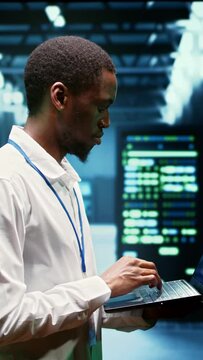 Vertical video African american engineer inspecting interlinked computers creating server network. High tech facility using parallel computing to perform complex calculations and process large amounts