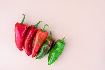 Different colored red green bell peppers in a row on beige background with copy space. Organic food, cultivating and harvesting eco vegetables