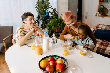 Mature lesbian couple feeding their adopted son at home