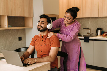 Young smiling indian woman giving massage her working husband