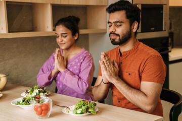Young indian couple praying before lunch together at home