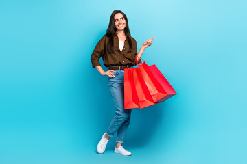 Full length photo of shopaholic fashionista young woman pointing finger empty space packages purchase isolated on blue color background