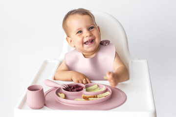 little cute girl eats complementary foods in a highchair, close up portrait on white background,...